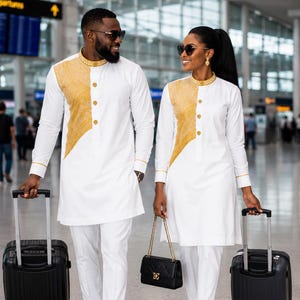 May include: Matching white long-sleeve tunics with gold textured panels on the chest, gold-trimmed collars, and gold buttons. The outfits are paired with white trousers, black loafers, and white heels, accompanied by black rolling suitcases and a black handbag.