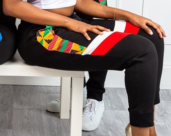 May include: Two people wearing black sweatpants with colorful patterned stripes down the sides. The woman is wearing a white tank top and gold heels. The man is wearing a black tank top and white sneakers.