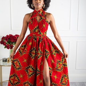 May include: A red maxi dress with a black and gold print. The dress has a halter neckline and a thigh-high slit. The model is wearing the dress with black heeled sandals.