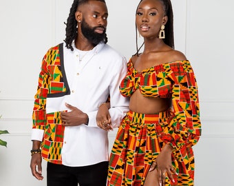 May include: A couple wearing matching outfits with a colourful geometric pattern. The man is wearing a white button-down shirt with a patterned sleeve and black trousers. The woman is wearing a crop top and a long skirt with a side slit.