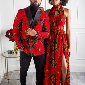 May include: A couple wearing matching red and black patterned outfits. The man is wearing a blazer with a black lapel and the woman is wearing a halter dress with a slit up the side.