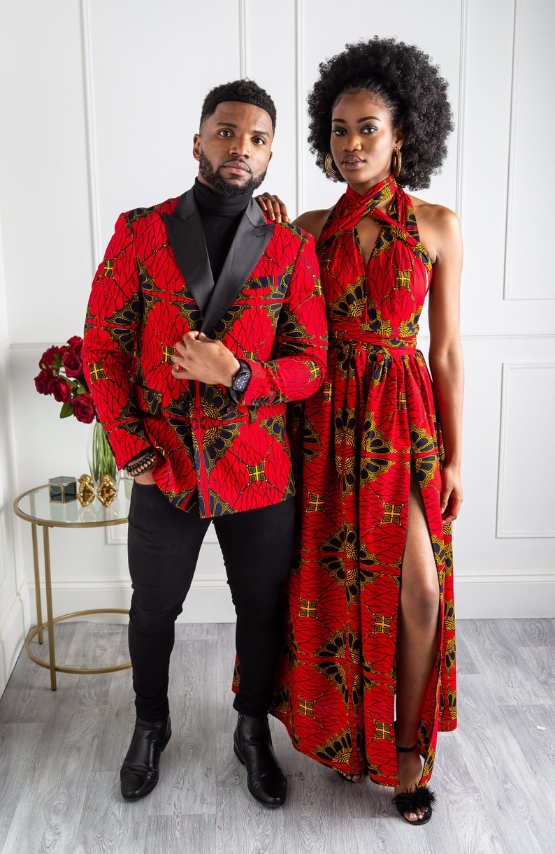 May include: A couple wearing matching red and black patterned outfits. The man is wearing a blazer with a black lapel and the woman is wearing a halter dress with a slit up the side.