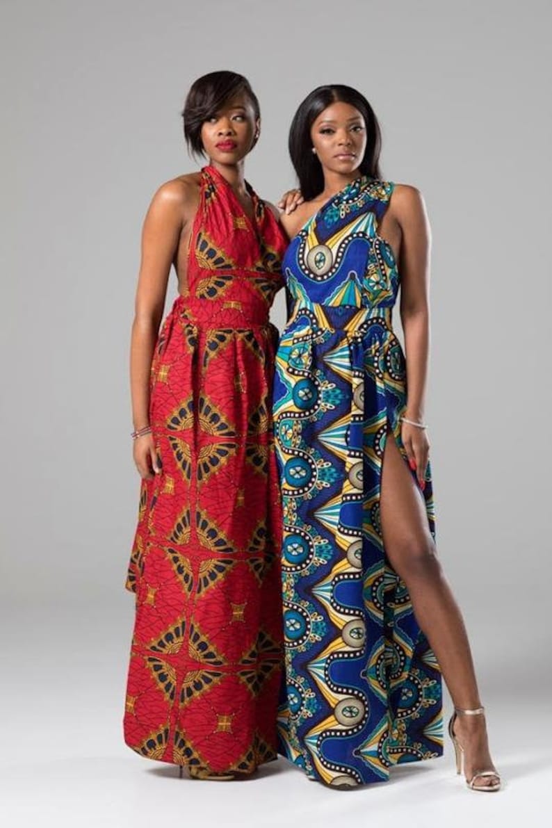 May include: Two women wearing long, colorful maxi dresses with geometric patterns. The dress on the left is red with gold accents, while the dress on the right is blue with yellow and green accents. Both dresses have a halter neckline and a side slit.