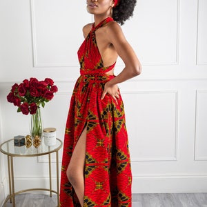 May include: A red maxi dress with a gold and black print. The dress has a halter neckline and a thigh-high slit. The model is wearing a matching head wrap.