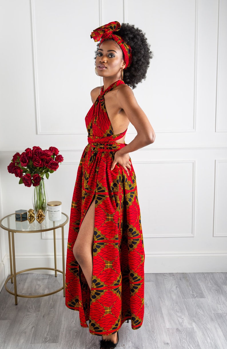 May include: A red maxi dress with a gold and black print. The dress has a halter neckline and a thigh-high slit. The model is wearing a matching head wrap.