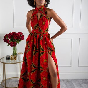 May include: A red maxi dress with a black and gold print. The dress has a halter neckline and a thigh-high slit. The model is wearing the dress with black heels.