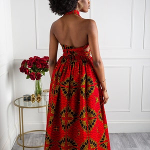 May include: A red maxi dress with a black and gold geometric print. The dress has a halter neckline and a tie at the back.