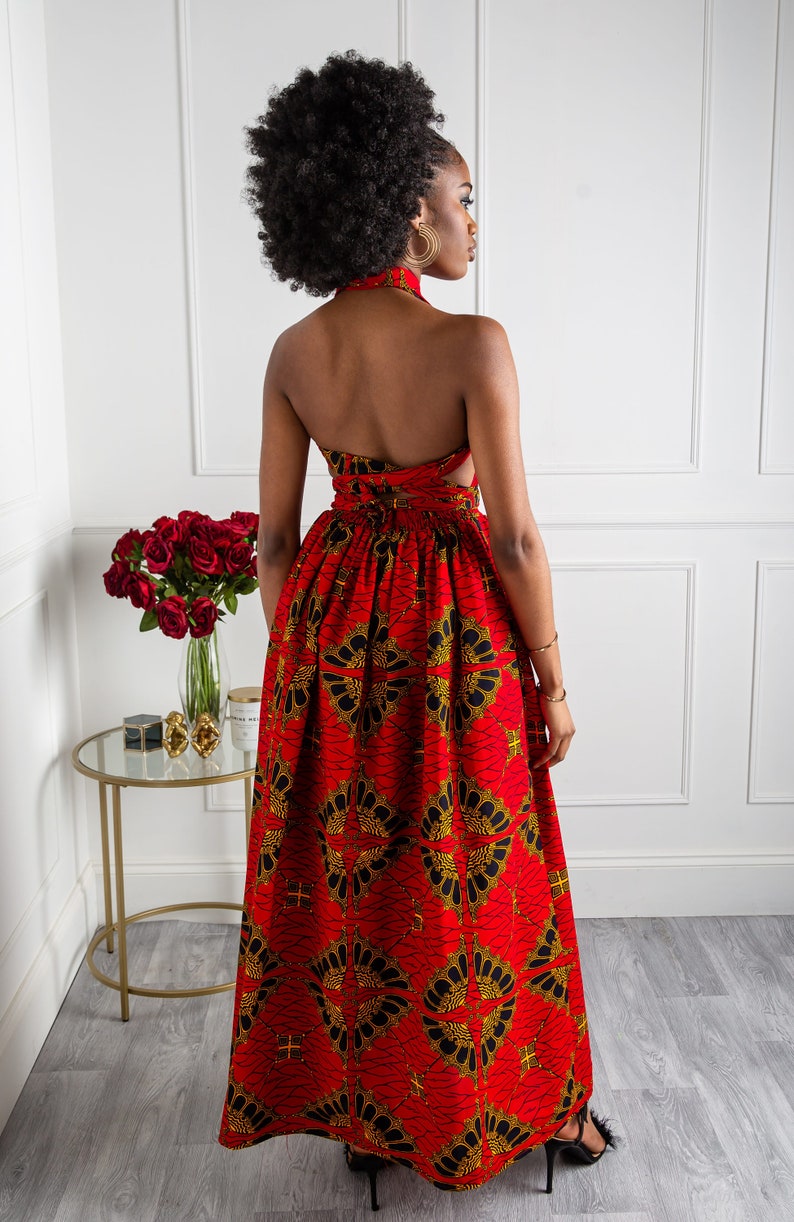 May include: A red maxi dress with a black and gold geometric print. The dress has a halter neckline and a tie at the back.