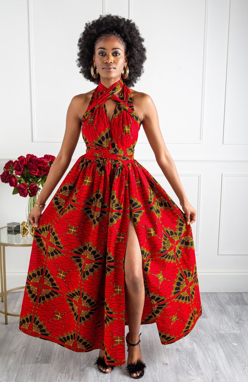 May include: A red maxi dress with a black and gold print. The dress has a halter neckline and a thigh-high slit. The model is wearing the dress with black heeled sandals.