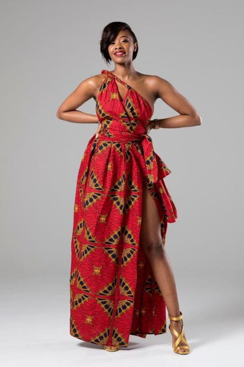 May include: A woman wearing a red and gold patterned maxi dress with a one-shoulder neckline and a thigh-high slit. The dress has a fitted bodice and a flowing skirt. She is wearing gold heels.