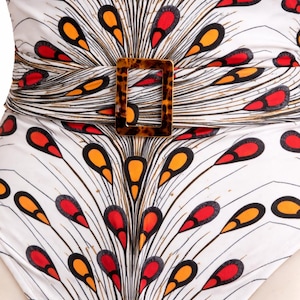May include: White swimsuit with a peacock feather design in red, orange, and black. It has a tortoiseshell-style buckle and a wrap-around waist. The swimsuit's design creates a flattering silhouette. The measurements are in centimeters.