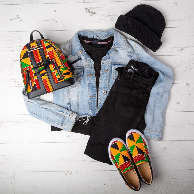 May include: A casual outfit featuring a light blue denim jacket, black jeans, a black beanie, and a black t-shirt. The outfit includes a colorful backpack and matching slip-on shoes with a geometric pattern in red, yellow, and green.