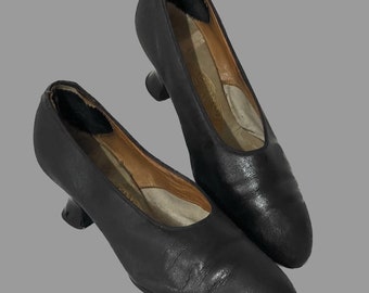 May include: A pair of black leather heeled shoes with a pointed toe. The shoes have a low heel and a simple design.