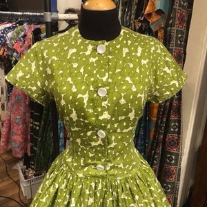 May include: A green and white floral print dress with a button-up front and short sleeves. The dress has a fitted bodice and a full skirt.