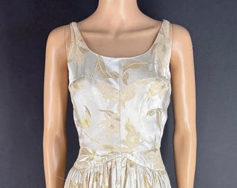 May include: A sleeveless, ivory-colored dress with gold floral embroidery. The dress features a scoop neckline and a fitted bodice that flares into a pleated skirt. The gold embroidery is concentrated on the bodice and skirt, creating a vintage aesthetic.