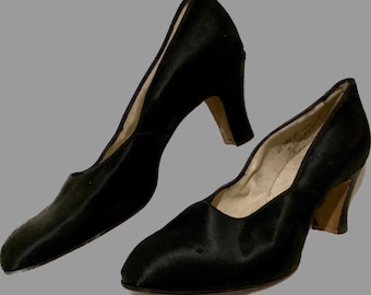 May include: A pair of black satin pumps with a low heel. The shoes have a rounded toe and a closed back.