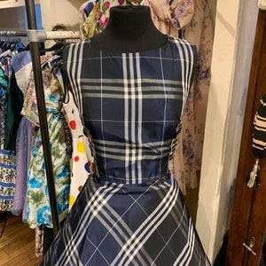 Op de afbeelding: Een marineblauwe en witte geruite jurk met een volle rok. De jurk is op een mannequin in een kledingwinkel.