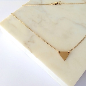 Op de afbeelding: Een gouden ketting met een klein, plat, gouden driehoekvormig hanger.