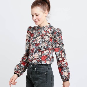 Könnte beinhalten: Eine weiße Keramik-Tasse mit schwarzem Henkel und dem Text "But First, Coffee" in fetter, schwarzer Schrift. Die Tasse steht vor einem verschwommenen Hintergrund, der eine gemütliche Umgebung suggeriert.