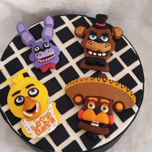 Könnte beinhalten: Ein runder Kuchen, der mit schwarz-weißem Schachbrettmuster verziert ist. Der Kuchen ist mit vier Fondantfiguren verziert: einem lila und blauen Bären, einem braunen Bären mit einem schwarzen Zylinder, einem gelben Küken mit einer rosa Lätzchen, auf dem "Let's Eat" steht, und einem braunen Bären, der einen Sombrero trägt.