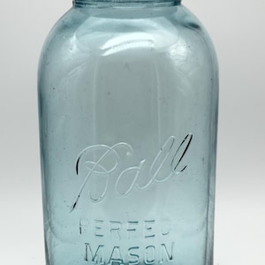Könnte beinhalten: Ein vintage Einmachglas aus blauem Glas mit Gewindehals und einem verwitterten Metalldeckel. Auf der Vorderseite befindet sich der geprägte Schriftzug Ball in Schreibschrift und PERFECT MASON in Blockschrift sowie eine kleine Zahl 21.