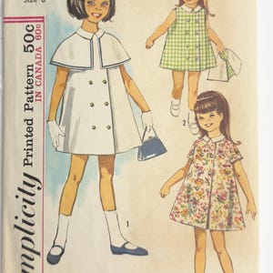 Könnte beinhalten: Ein Vintage-Schnittmusterumschlag von Simplicity, Nummer 5427 für Kindergröße 6, mit Illustrationen von drei verschiedenen Kleiderstilen. Die Entwürfe umfassen ein zweireihiges Mantelkleid mit Kragen, ein ärmelloses kariertes Kleid und ein geblümtes Kleid.