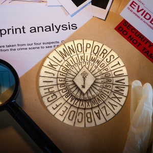 May include: A close-up of a wooden alphabet cipher wheel with a keyhole in the center. The wheel is surrounded by a brown surface and white latex gloves. The text "SECURITY SEAL DO NOT TAMPER" is visible on a red label.