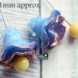 May include: Two blue glass flower beads with gold trim and a yellow bead centre. The beads are approximately 1.8 x 2.1 cm. The Glass Cavern logo is in the lower right corner. The text "18x21mm approx" is at the top.