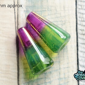 May include: Two glass beads, approximately 25mm in size, with a gradient of purple, gold, and green colours. The beads have a textured, bubbly surface.