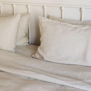 May include: A bed with a white metal headboard and light beige linen bedding. The bedding includes two large pillows and a fitted sheet, creating a soft and inviting aesthetic. The neutral color palette suggests a calming bedroom environment.
