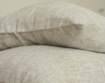 May include: Two light beige linen pillows stacked on top of each other. The pillows have a textured appearance and are made of a natural fabric. The pillows are on a light beige surface.