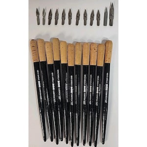 Könnte beinhalten: Eine Sammlung von Kalligraphie-Stiften und -Federn. Die Stifte haben schwarze Griffe mit Korkgriffen und den Text "1015 EAGLE CORTEX USA". Die Federn sind silberfarben und in verschiedenen Formen. Die Artikel sind auf einer weißen Oberfläche angeordnet.