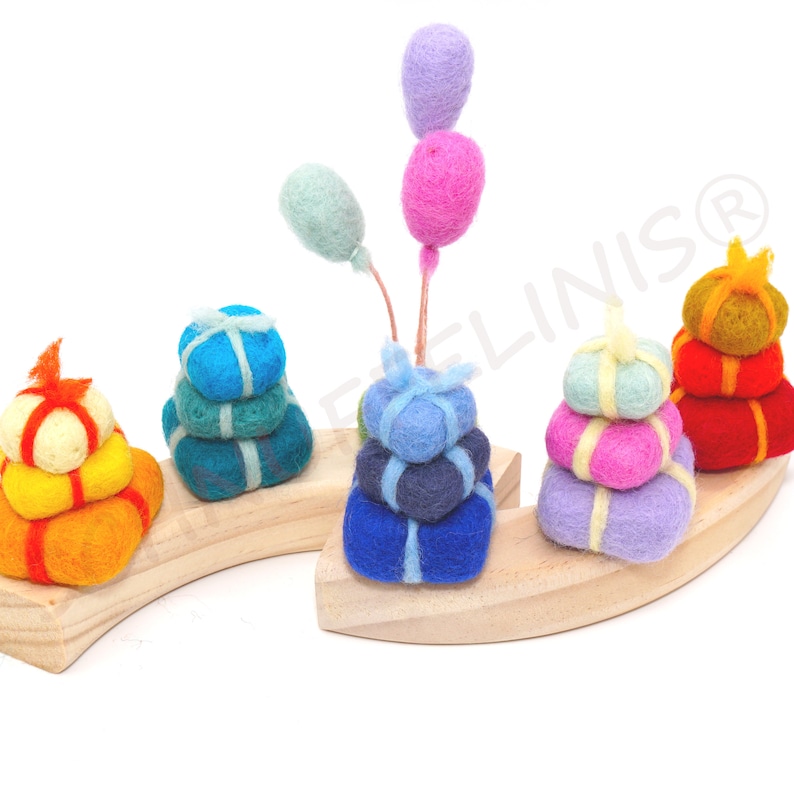 Op de afbeelding: Een houten stapelspel met viltstukken in de vorm van cadeaus en ballonnen. De cadeaus zijn gestapeld in verschillende kleuren, waaronder blauw, groen, geel, roze en paars. De ballonnen zijn lichtblauw en roze.