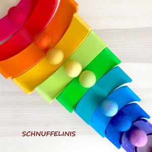 May include: A rainbow-colored wooden arch toy with felt balls. The arches are stacked in a pyramid shape, with the largest arch at the bottom and the smallest arch at the top. The felt balls are in various colors, including red, orange, yellow, green, blue, and purple.