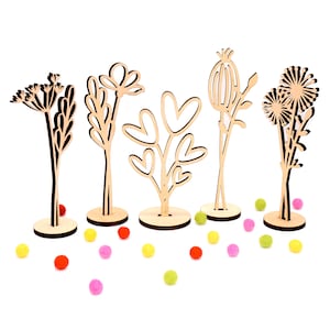 Op de afbeelding: Vijf houten bloemen uitsnijdingen met verschillende ontwerpen, waaronder harten, een paardenbloem en een bloem met een enkele bloei. De uitsnijdingen staan op een wit oppervlak met kleurrijke pompoenen die eromheen zijn verspreid.