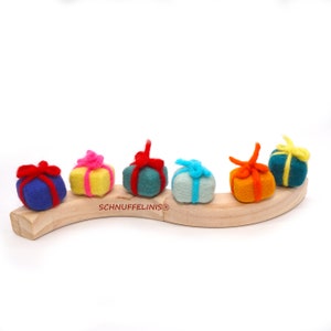 May include: Six felt gift boxes in various colors, including blue, yellow, green, orange, and teal, are lined up on a wooden curved surface. The boxes have red ribbons and are arranged in a row.