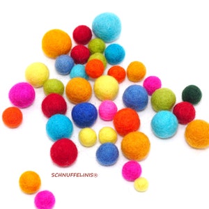 May include: A collection of multi-colored felt balls in various sizes, including shades of red, orange, yellow, green, blue, and pink. The text SCHNUFFELINIS is printed in red near the bottom center of the arrangement of these round spheres.