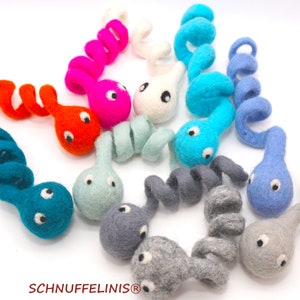 May include: A collection of ten colorful felt toy tadpoles. Each tadpole is a different color, including blue, green, pink, orange, and gray. The tadpoles are curled into a spiral shape and have black eyes.