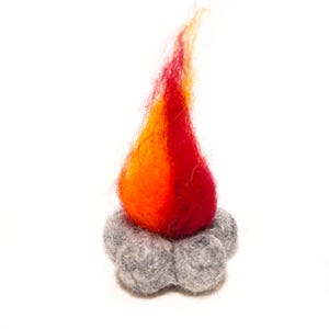 Pode incluir: Uma escultura artesanal de fogueira em feltro. A chama é uma mistura vibrante de vermelho, laranja e amarelo, sobre uma base de 'troncos' de feltro cinza. O feltro é texturizado, dando à fogueira uma aparência realista. A escultura está em um fundo branco.