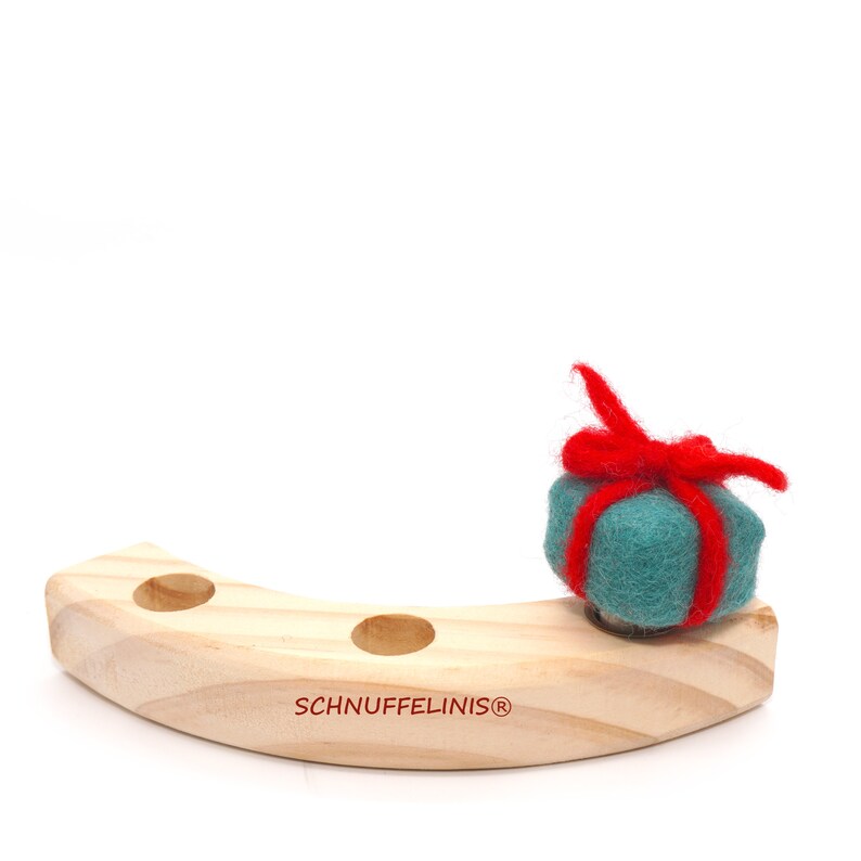 May include: A wooden, crescent-shaped stand with three holes, featuring the text "SCHNUFFELINIS&reg;". A teal felt gift box with a red felt bow sits on the stand.