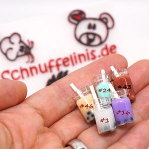 Könnte beinhalten: Fünf Miniatur-Glasflaschen mit Strohhalmen, gefüllt mit verschiedenen farbigen Flüssigkeiten und Boba-Perlen. Die Flaschen sind mit Nummern gekennzeichnet: #46, #24, #43, #1 und #16.