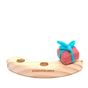 May include: A wooden toy with three holes and a felt gift box with a blue ribbon on top. The toy is labeled "Schnufelinis&reg;".