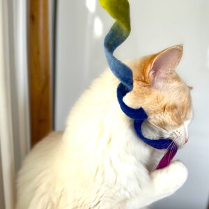 以下が含まれることがあります： 白とオレンジの猫が青と黄色のフェルトのおもちゃで遊んでいます。猫はおもちゃを見て、口を開けています。