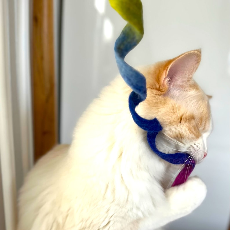 以下が含まれることがあります： 白とオレンジの猫が青と黄色のフェルトのおもちゃで遊んでいます。猫はおもちゃを見て、口を開けています。