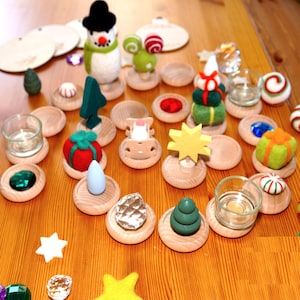 May include: A collection of Christmas ornaments and decorative items on a wooden surface. The ornaments include a snowman, a cow, a star, a Christmas tree, and various other festive shapes. There are also small glass candle holders and wooden discs.