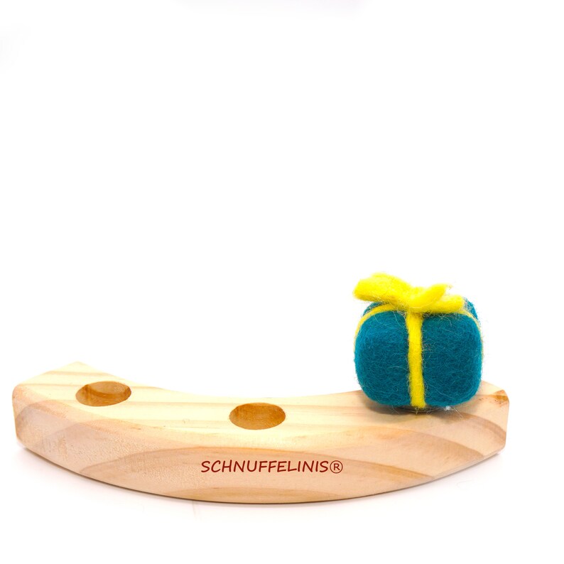 May include: A teal felt gift box with a yellow ribbon sits on a wooden rolling toy with the text "SCHNUFFELINIS&reg;" on the bottom.