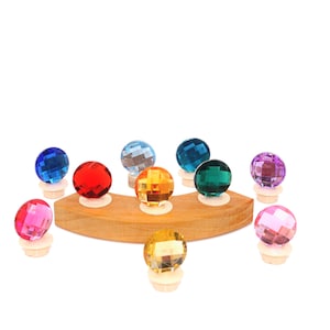 Op de afbeelding: Een verzameling kleurrijke, facetgeslepen glazen flessenstoppers in diverse kleuren, waaronder blauw, rood en groen. De stoppers zijn op een houten display geplaatst, wat hun juweelachtige uiterlijk benadrukt. Elke stopper heeft een diameter van ongeveer 2,5 cm.