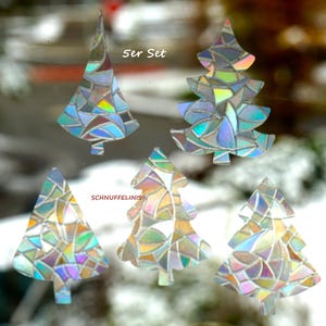 Könnte beinhalten: Set aus fünf Fensteraufklebern in Form von Christbäumen mit schillerndem Effekt. Jeder Baum besteht aus kleinen, farbigen, geometrischen Formen. Der Text "5er Set" befindet sich oben links und "SCHNUFFELINIS®" unten links.