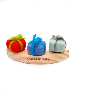 May include: Three felt gift boxes in red, blue, and green, with matching ribbon, are arranged on a wooden rocking horse. The horse is labeled "Schnufelinis&reg;".
