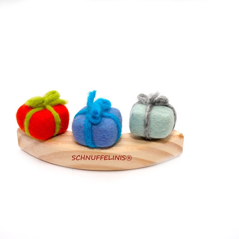 May include: Three felt gift boxes in red, blue, and green, with matching ribbon, are arranged on a wooden rocking horse. The horse is labeled "Schnufelinis&reg;".